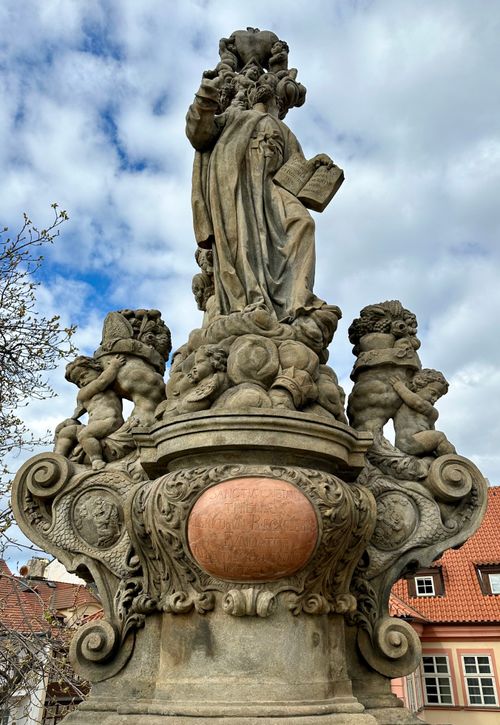 Free Intricate Baroque statue with cherubs on Charles Bridge, Prague, surrounded by vibrant architecture. Stock Photo