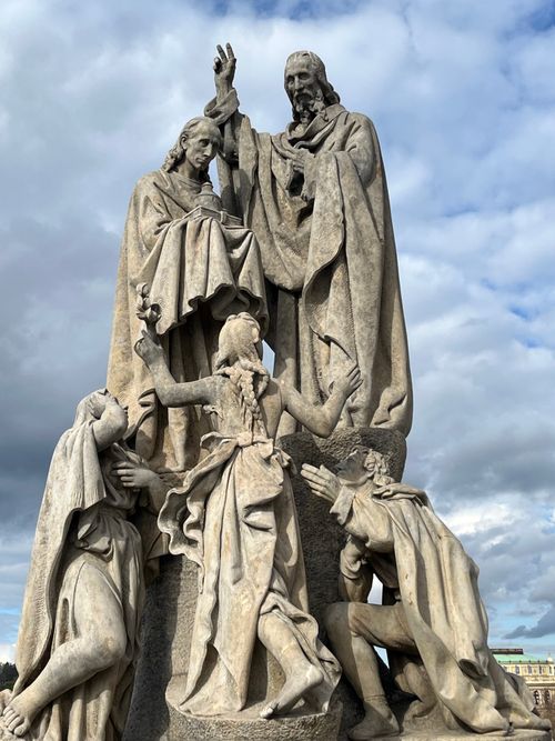 Free Intricate Baroque statues depicting a religious scene on Charles Bridge, Prague under a cloudy sky. Stock Photo