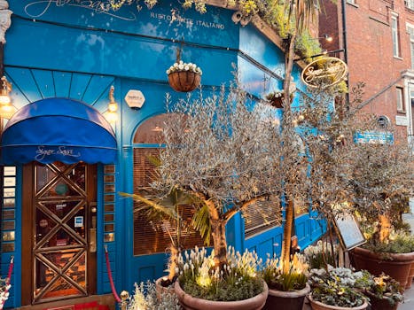 Vibrant blue Italian restaurant facade adorned with lush potted plants, evening lights creating a warm ambiance.