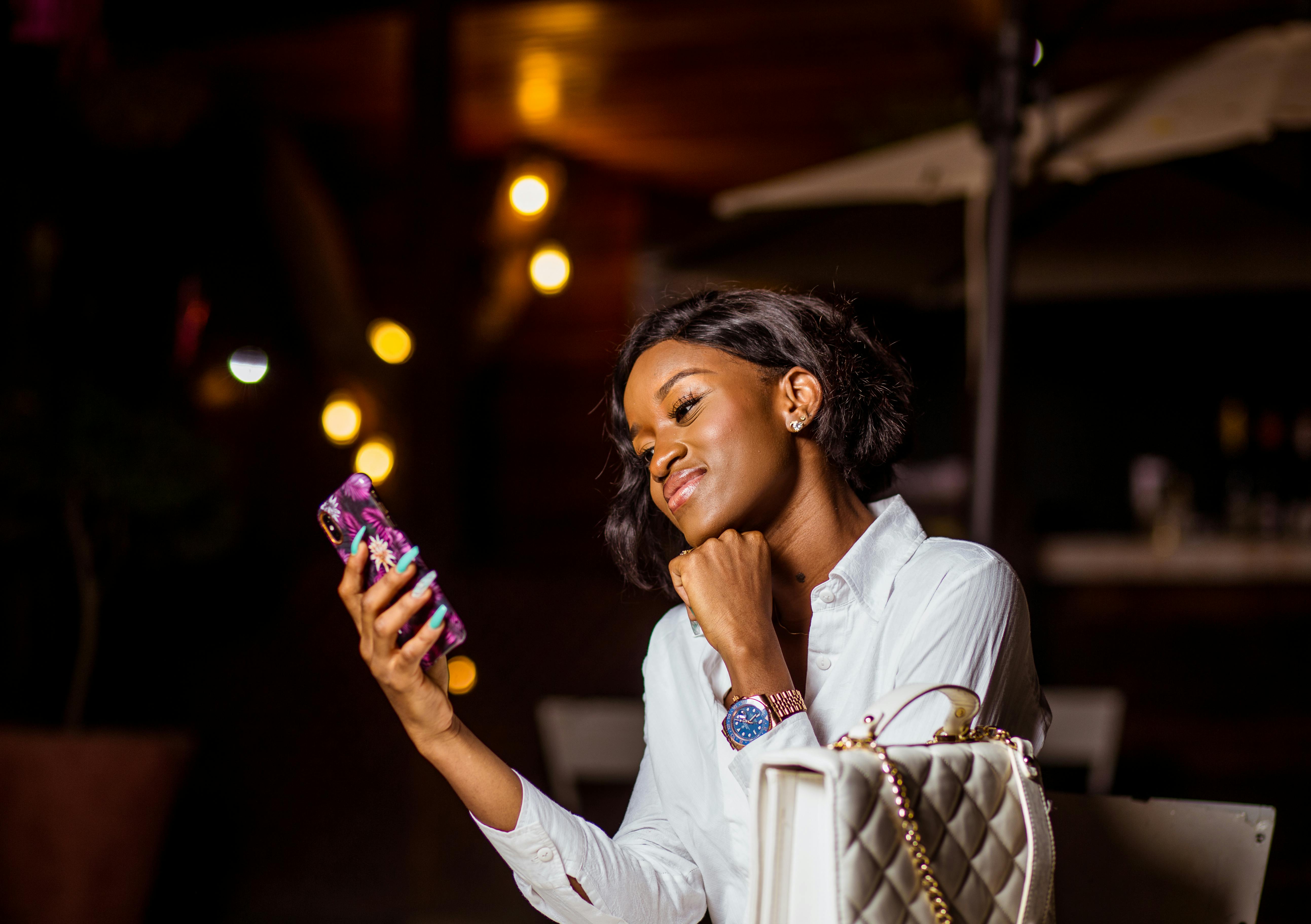 一名身穿白色上衣的女子在晚灯下对着手机微笑