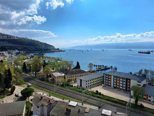 Free A panoramic view of a seaside town with lush greenery, buildings, and ships in the harbor under a bright sky. Stock Photo