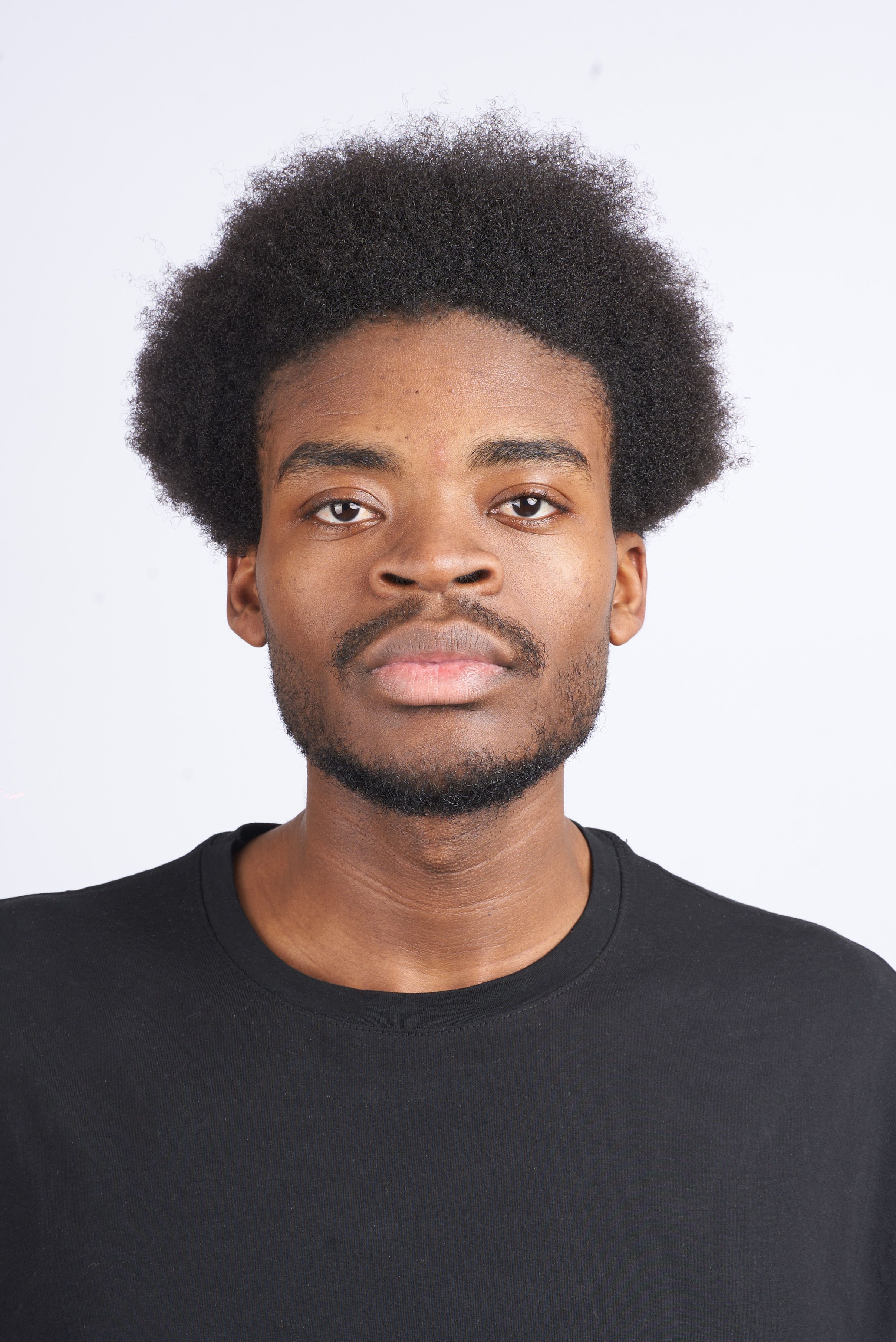 Professional studio portrait of a man with afro hair wearing a black t-shirt against a white backdrop.