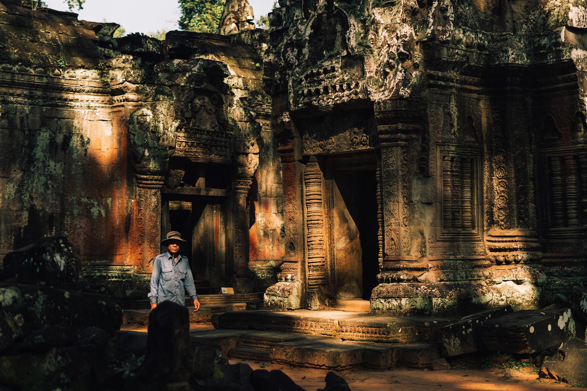 A visitor explores the ancient Ta Prohm Temple in Siem Reap, Cambodia surrounded by intricate stone carvings.