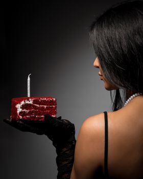 A woman with a piece of red velvet cake topped with a candle, creating a dramatic and elegant birthday scene.