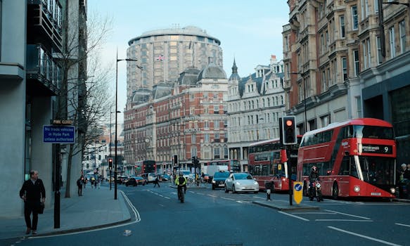 Street scene in London featuring iconic red buses, historic buildings, and urban life.