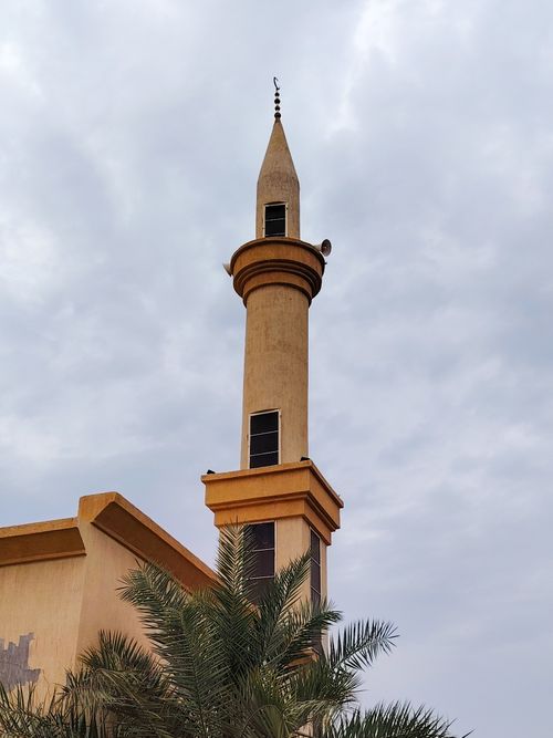 Free A beautiful mosque minaret set against a cloudy sky, surrounded by palm trees. Stock Photo