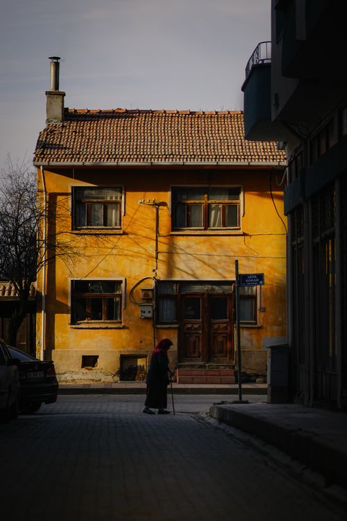 Free An elderly person walks past a vintage yellow house on a quiet street at dusk. Stock Photo