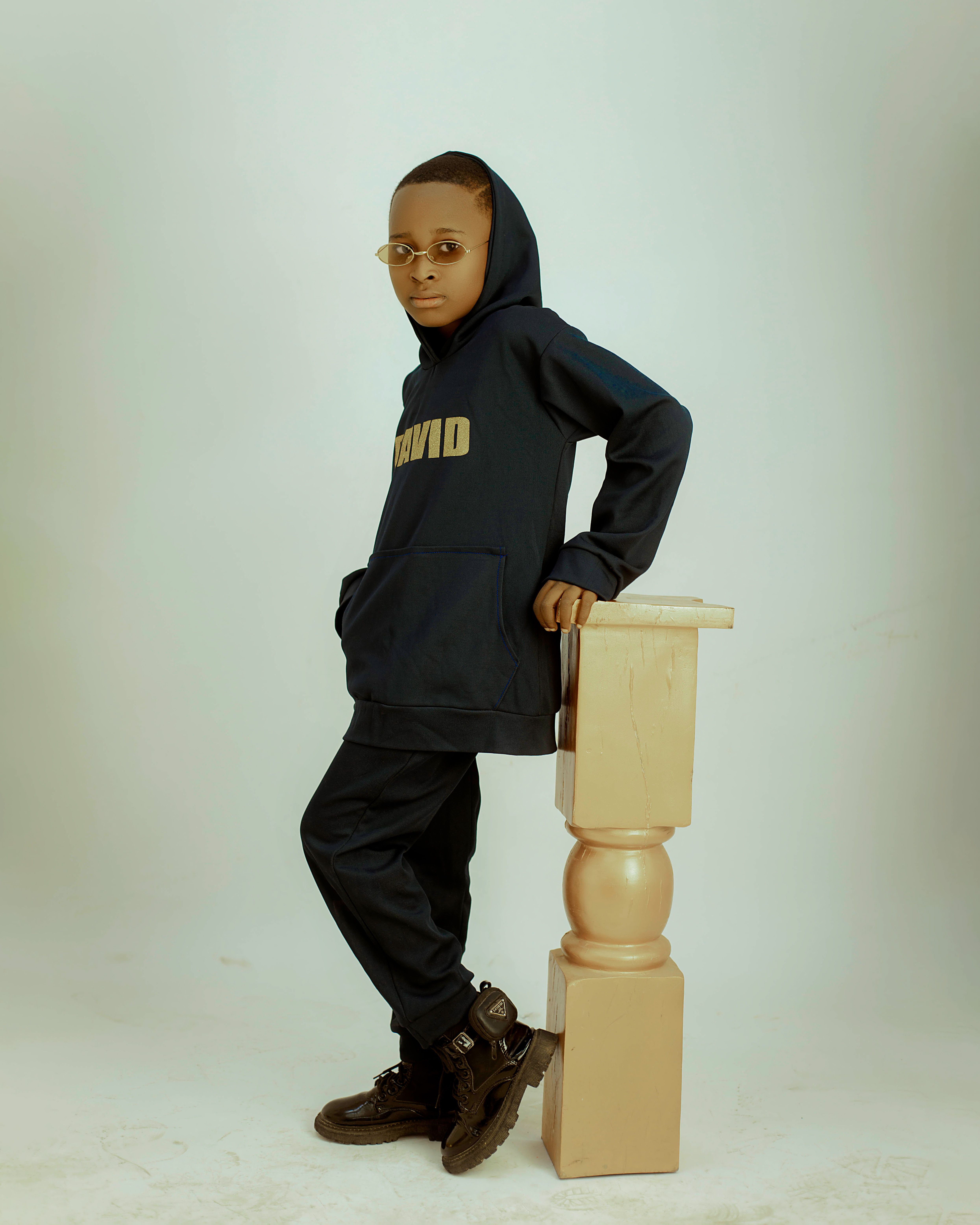 A fashionable young boy poses in a hoodie and sunglasses, showcasing cool style.