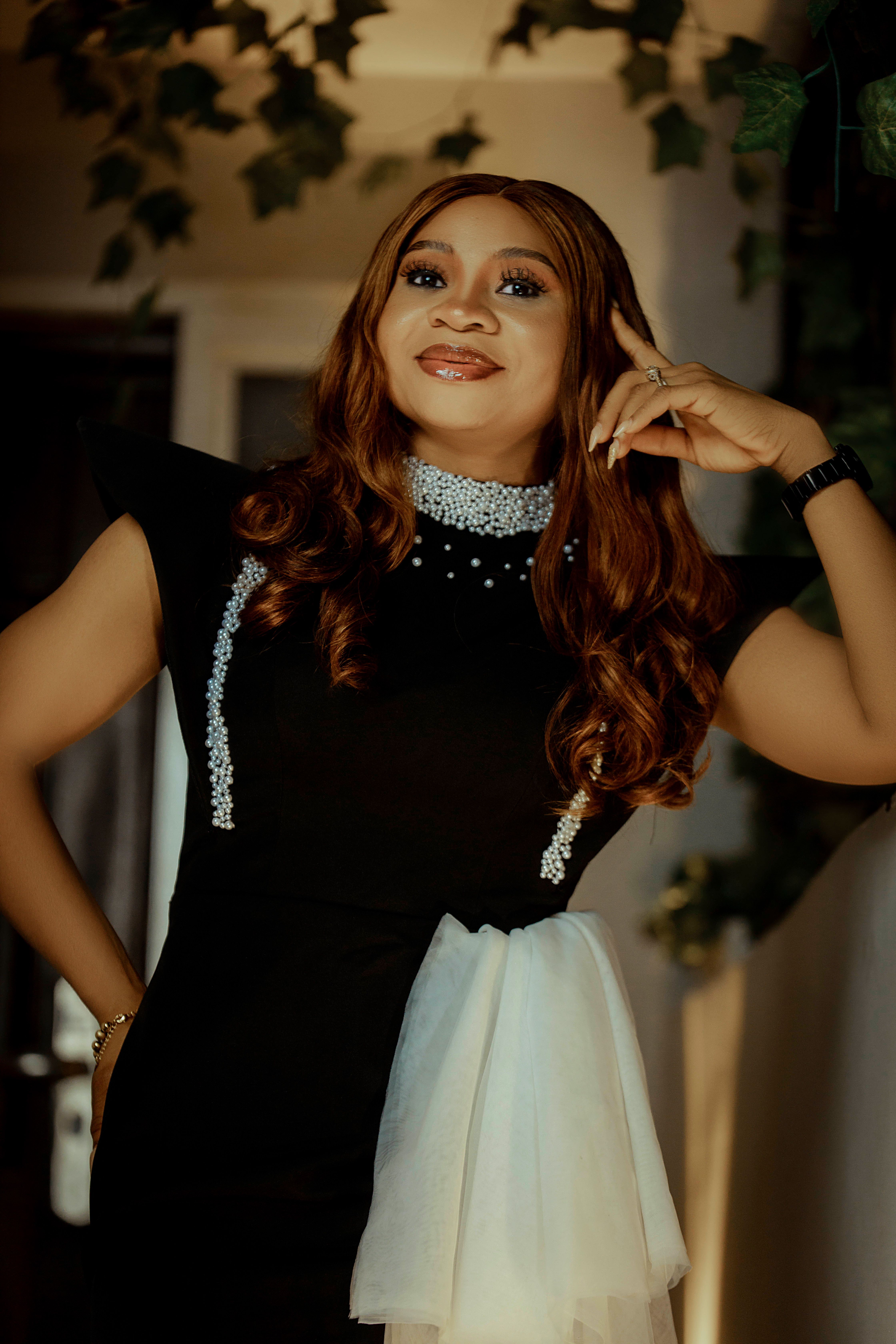 A fashionable woman poses confidently in an elegant black dress indoors.