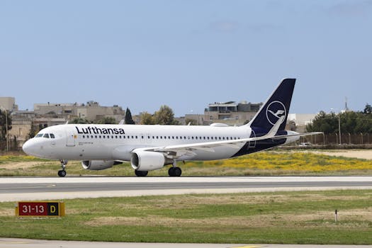 Lufthansa Airbus A320 taxiing on runway with clear sky and city backdrop.