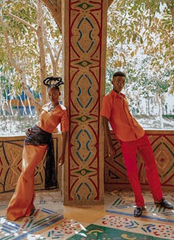 Colorful portrait of two adults in striking outfits against an ornate backdrop.