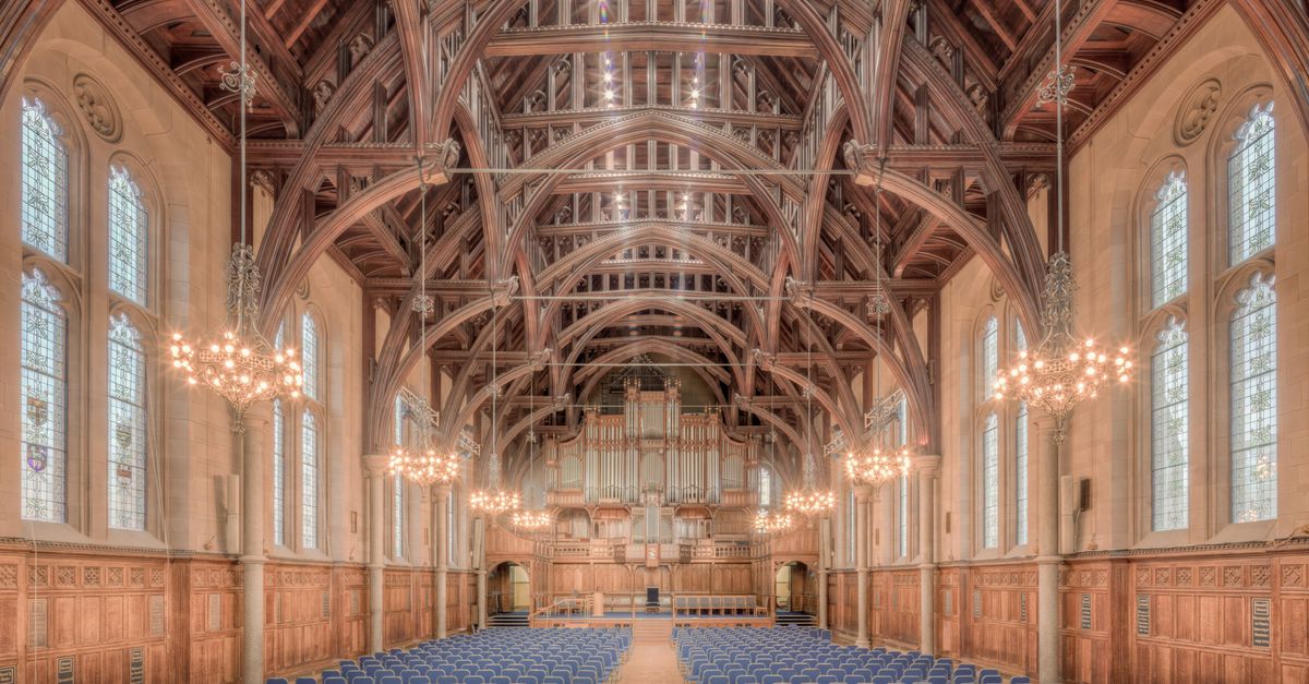 Elegant interior of a historic hall at the University of Manchester, showcasing intricate wooden beams and lighting.