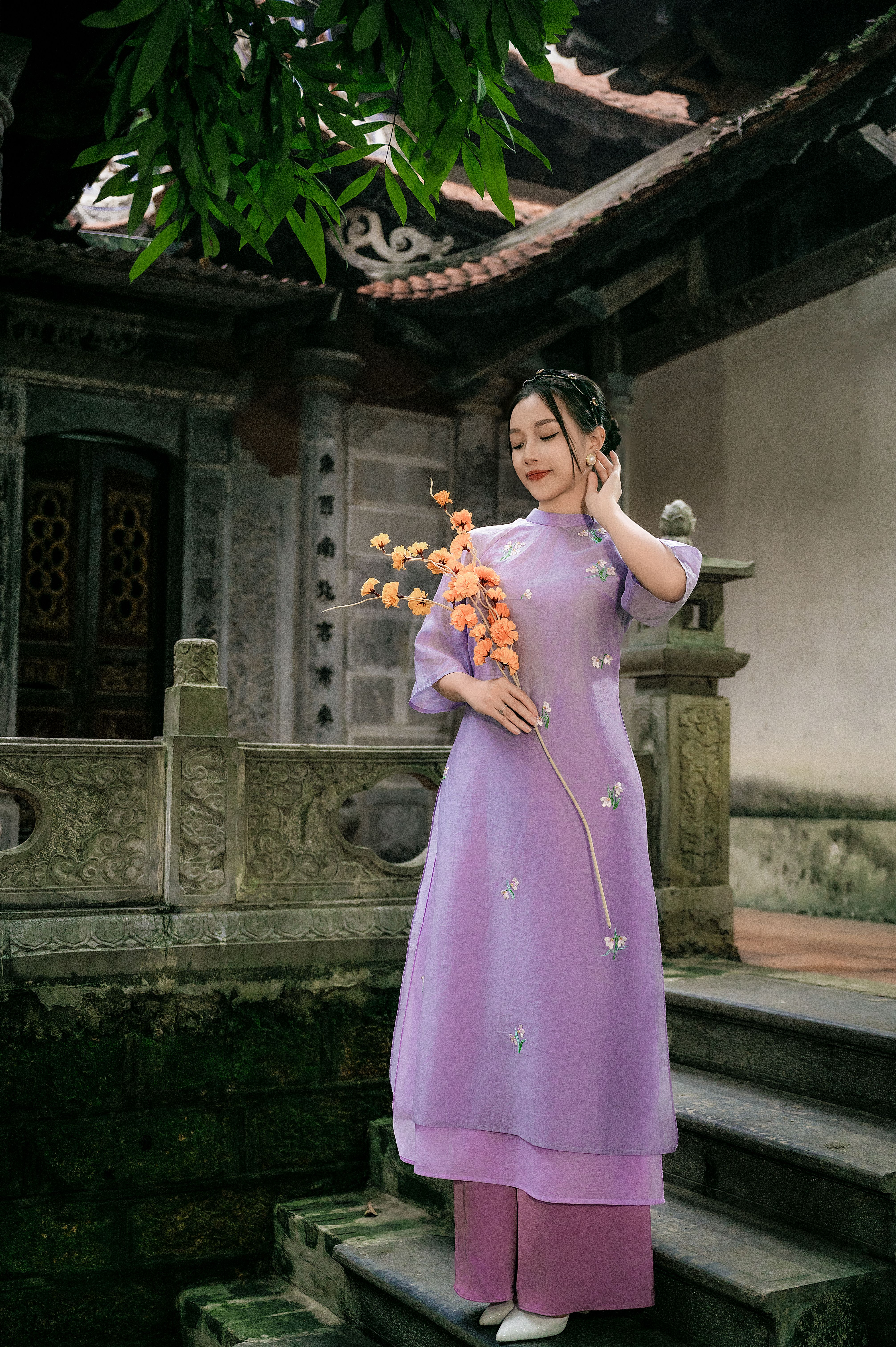 Woman in traditional dress holding orange flowers, posing on historic steps.