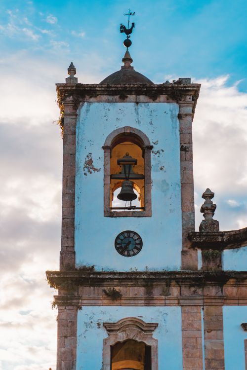 Free A charming historic church bell tower with a clock against a bright, cloudy sky. Stock Photo