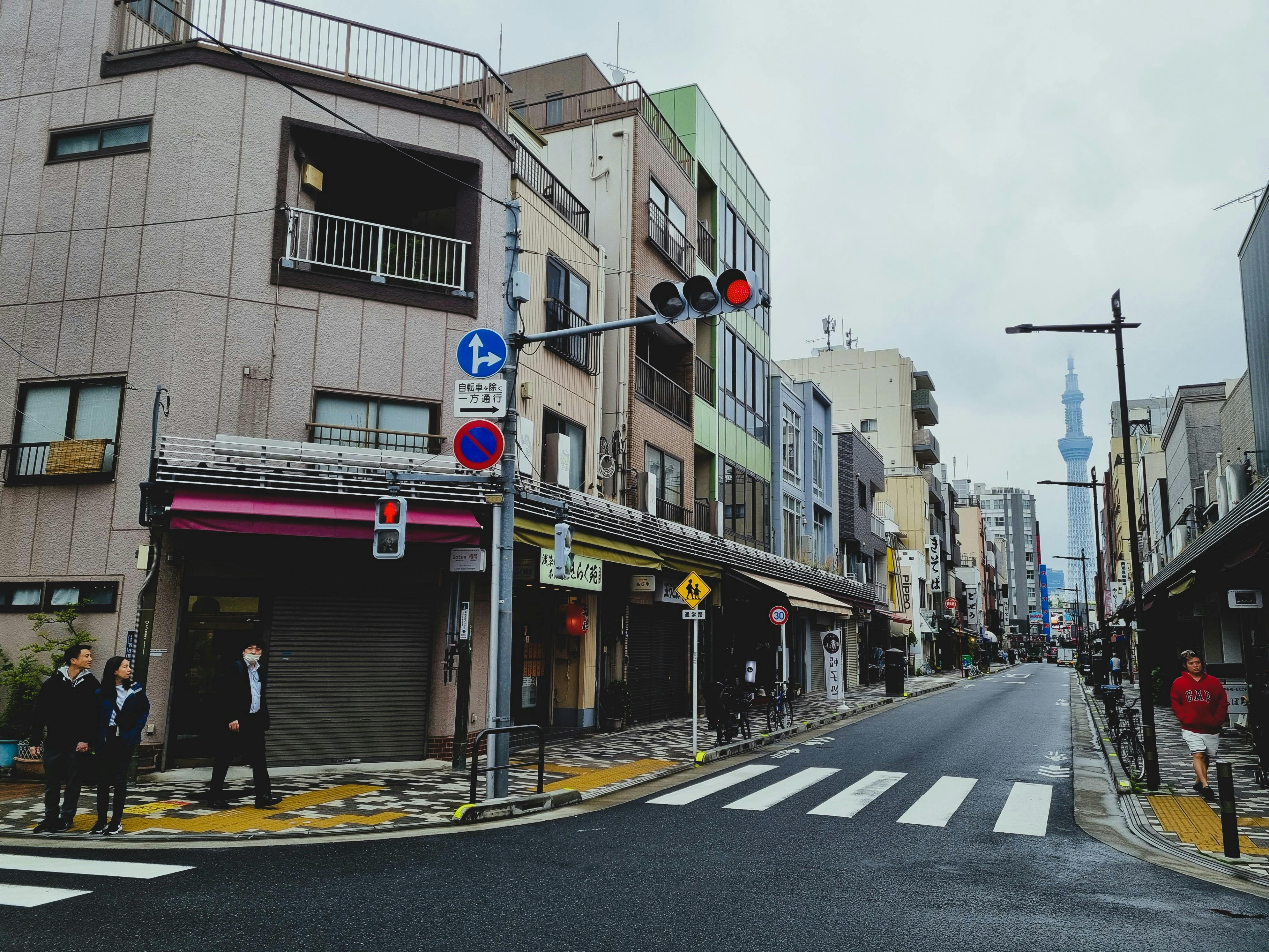 Street scene in Tokyo with pedestrians and the iconic Tokyo Skytree visible in the distance.