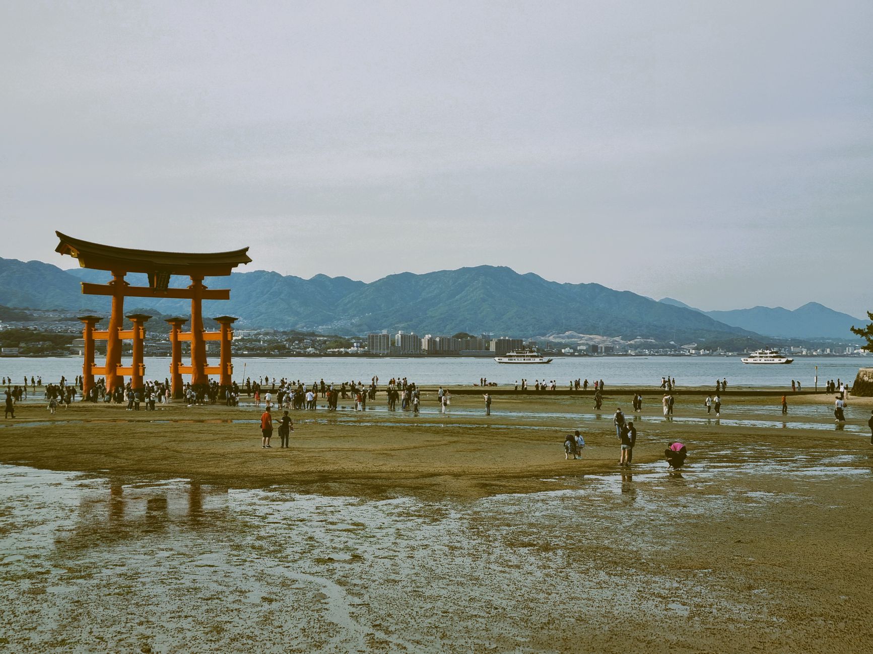 Tourists walking near the iconic floating Torii gate at Itsukushima Shrine, Japan.