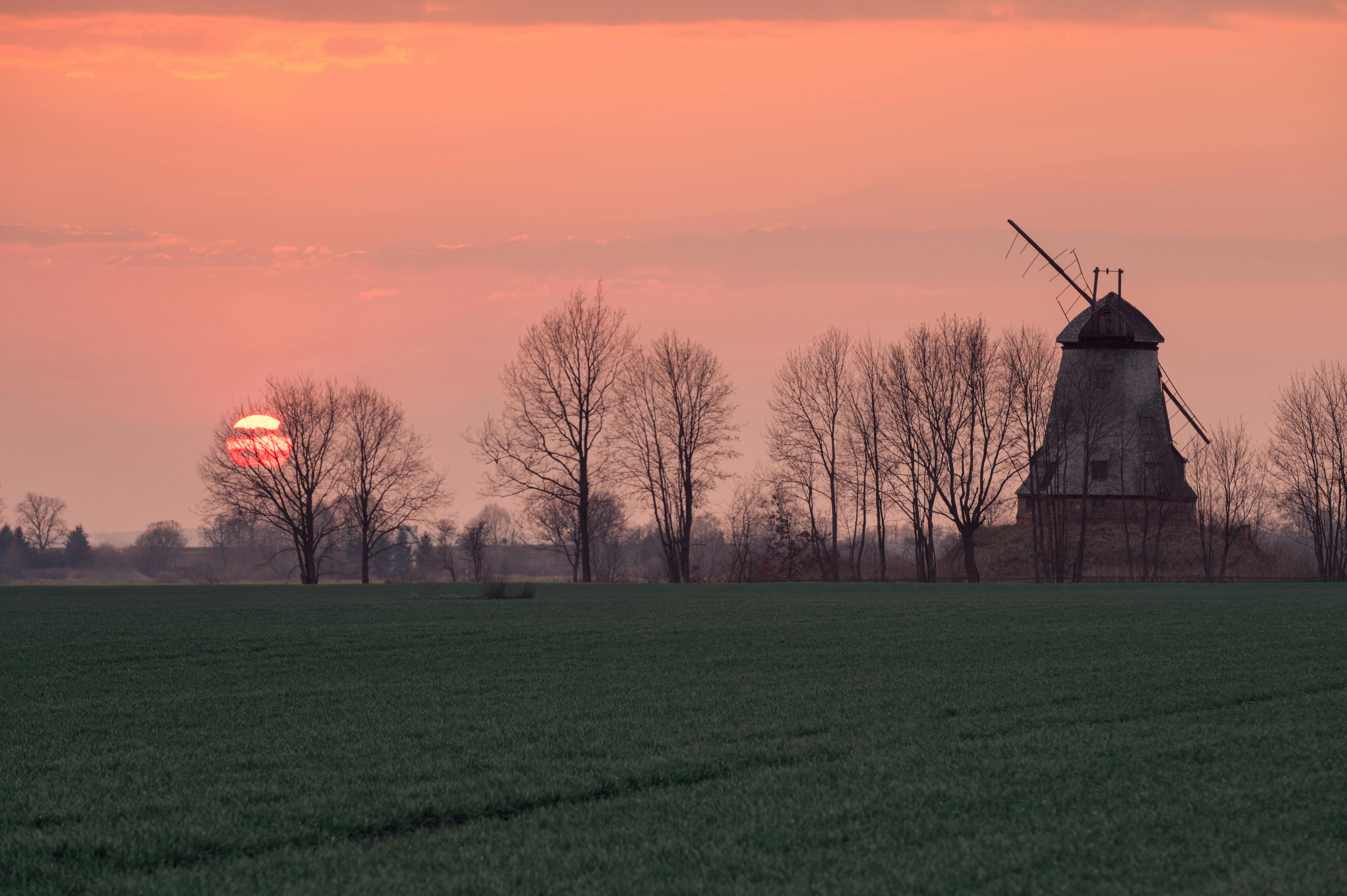 Scenic view of a sunset over a rural windmill and trees in Palczewo, Poland.