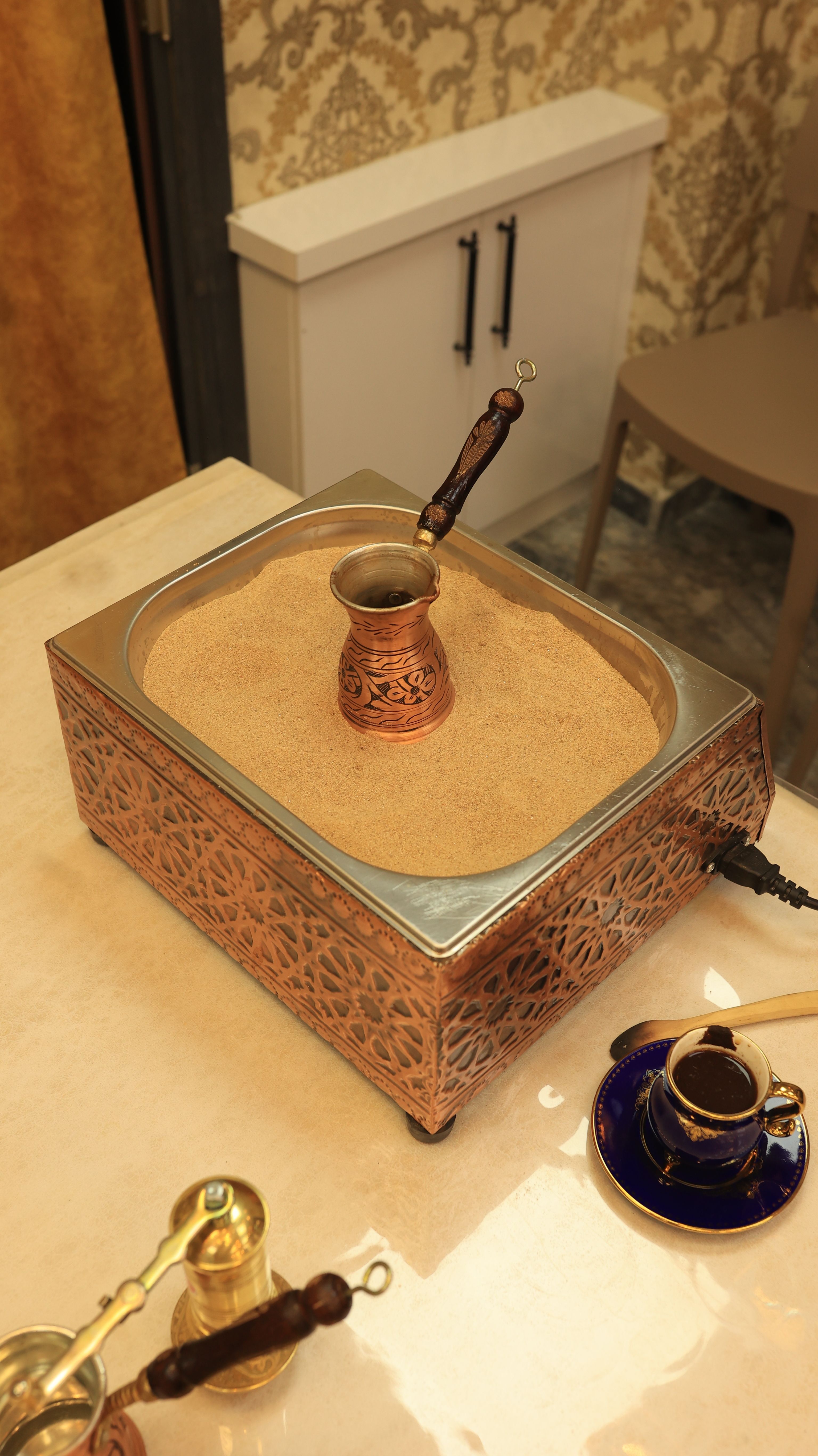 Turkish coffee being prepared on traditional sand heater with copper pot.