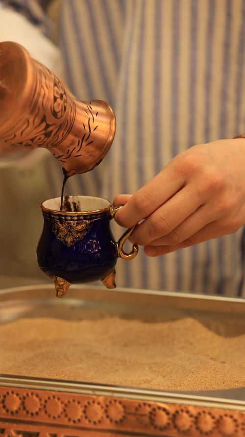 Free Hand pouring rich Turkish coffee from a copper pot into a decorative cup, showcasing cultural coffee traditions. Stock Photo
