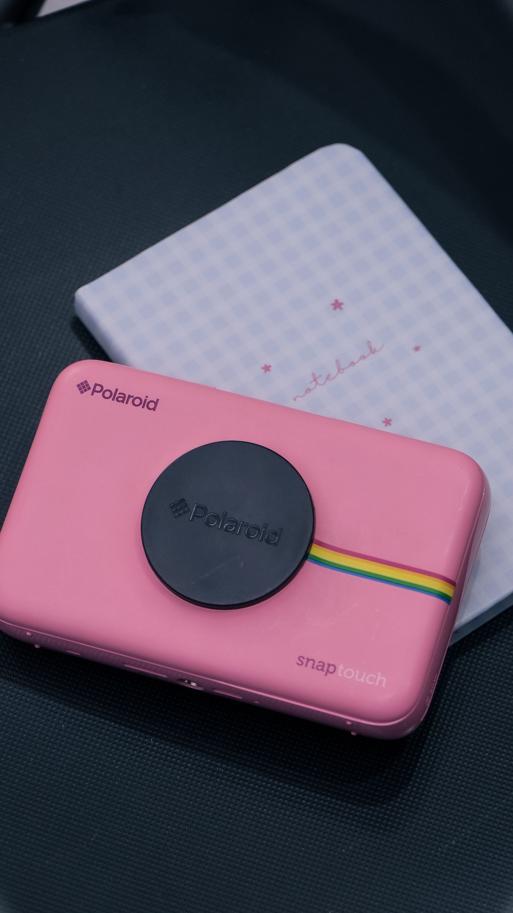 Pink Polaroid Snap Touch camera on a dark surface with a notebook.