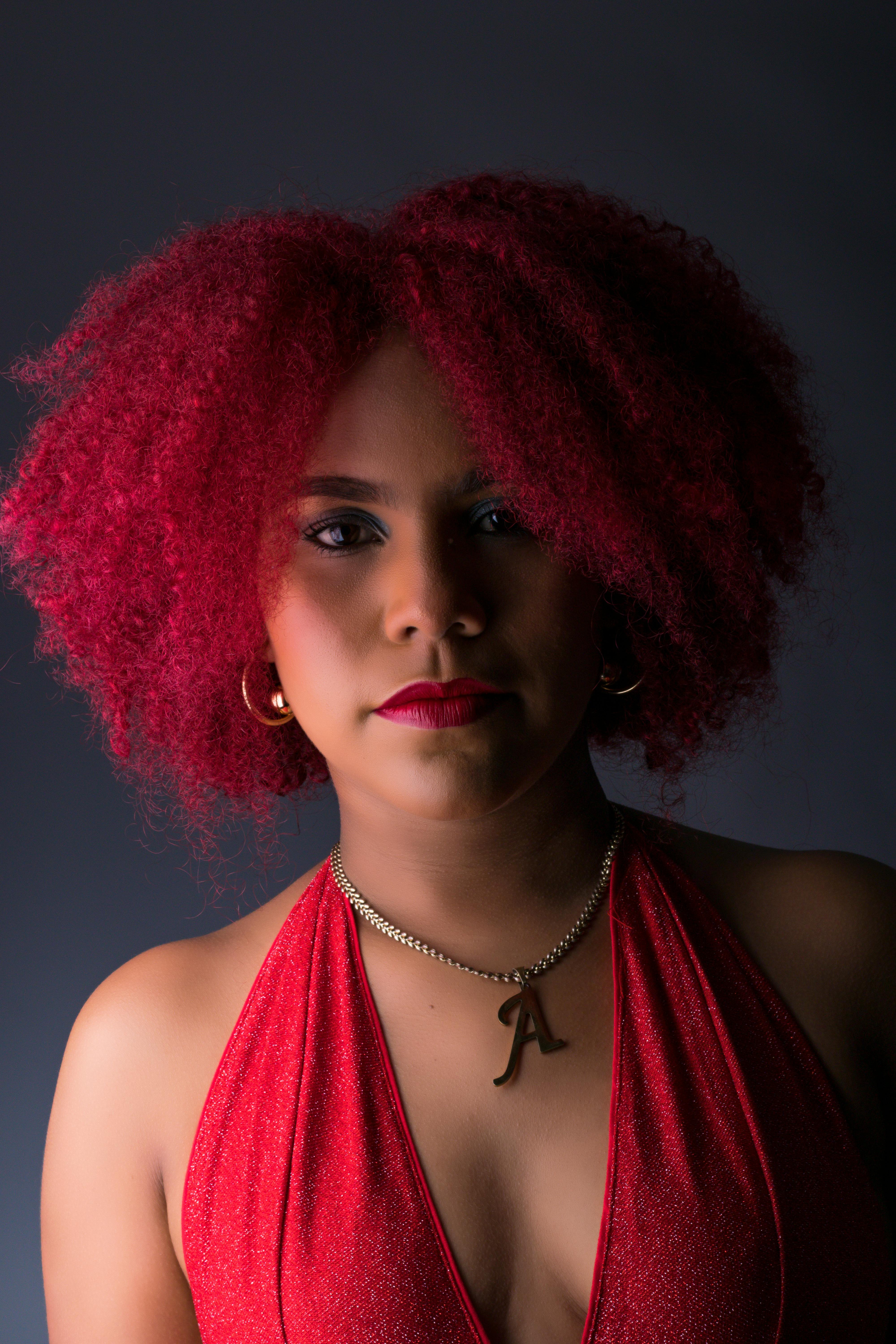 Stylish portrait of a woman in a red dress, showcasing her vibrant curly hair against a dark background.