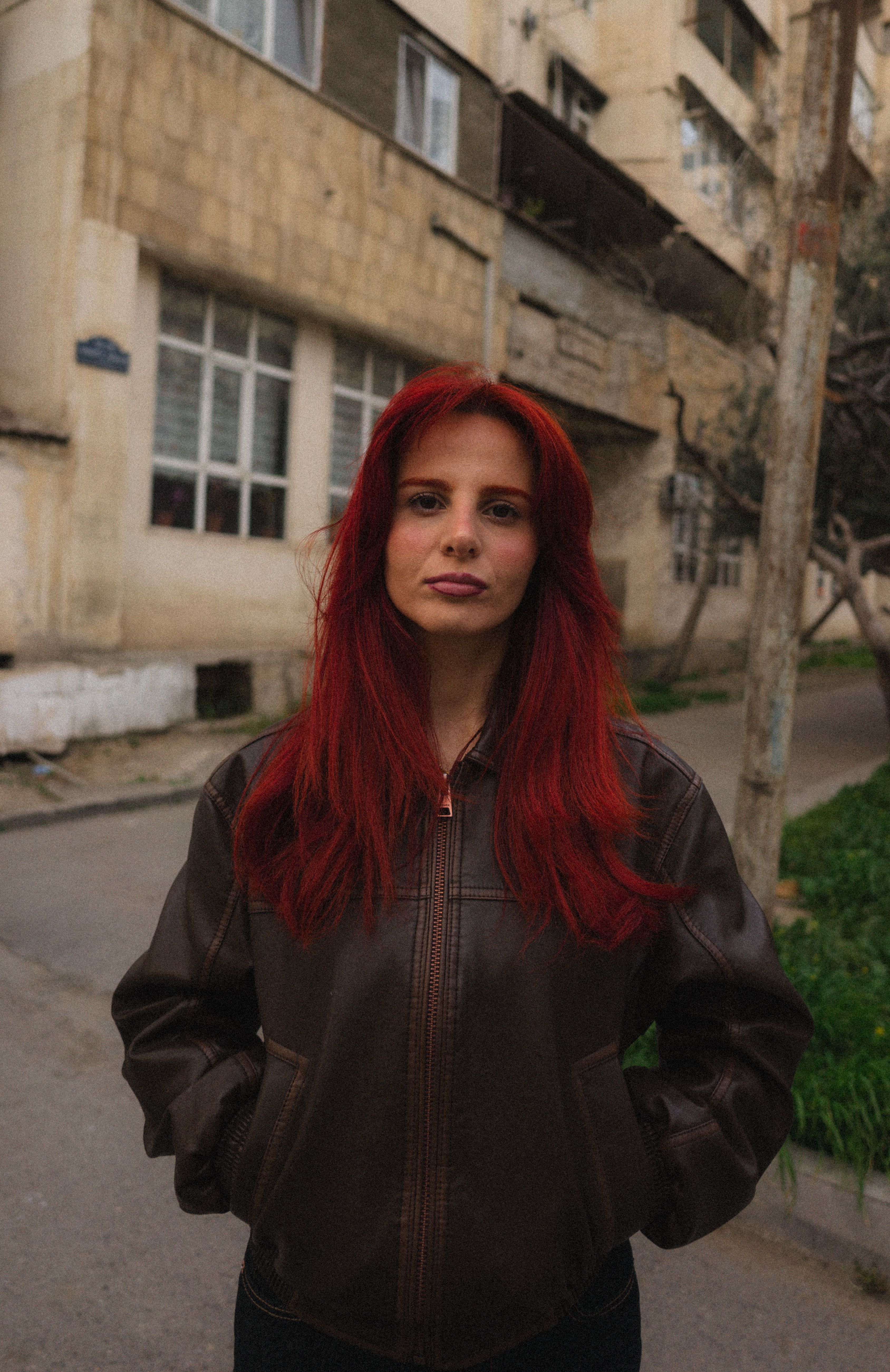A woman with red hair in a leather jacket standing on a street in Baku, Azerbaijan.