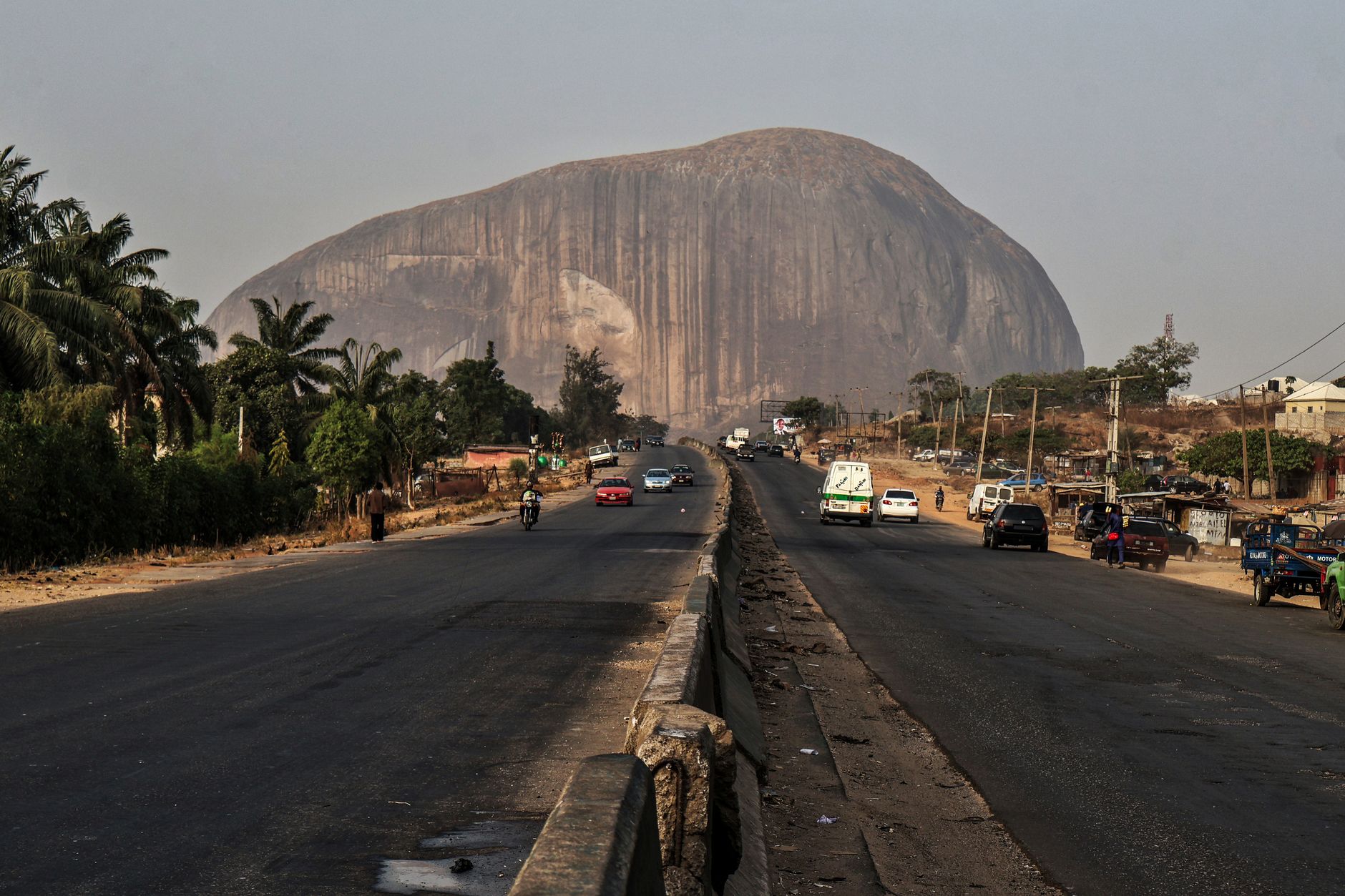 Capture of the iconic Zuma Rock with a bustling road in Abuja, Nigeria during the day.