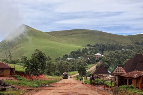 Free Idyllic rural village scene with lush green hills and dirt road. Stock Photo