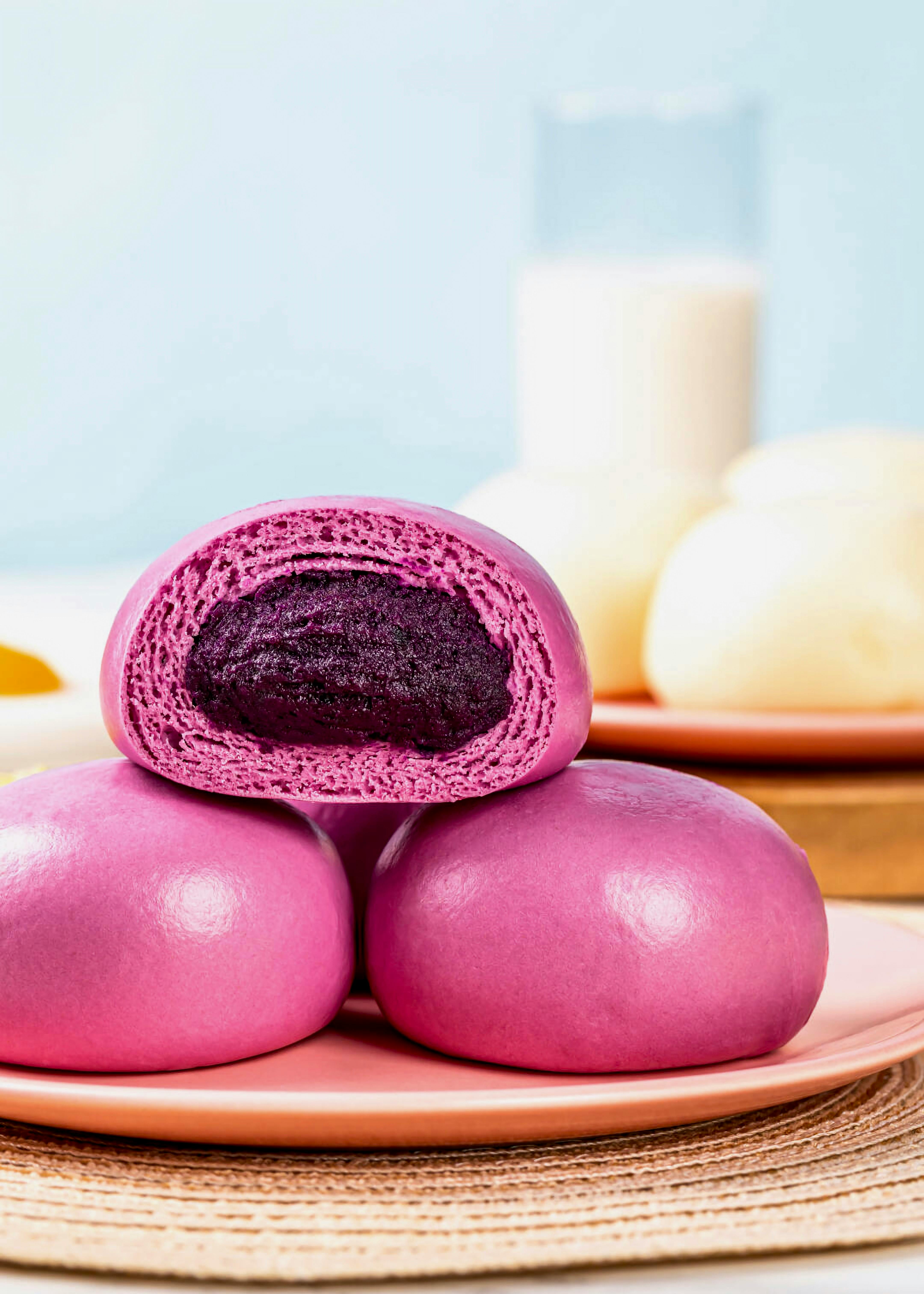 Bright purple buns filled with ube paste, served with milk in a soft and vibrant setting.