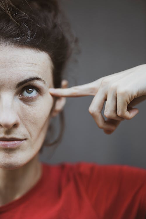 Selective Focus Portrait Photo of Woman in Red T-shirt Pointing to Her Head