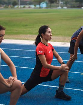 Group of adults doing stretching exercises on a track field outdoors.