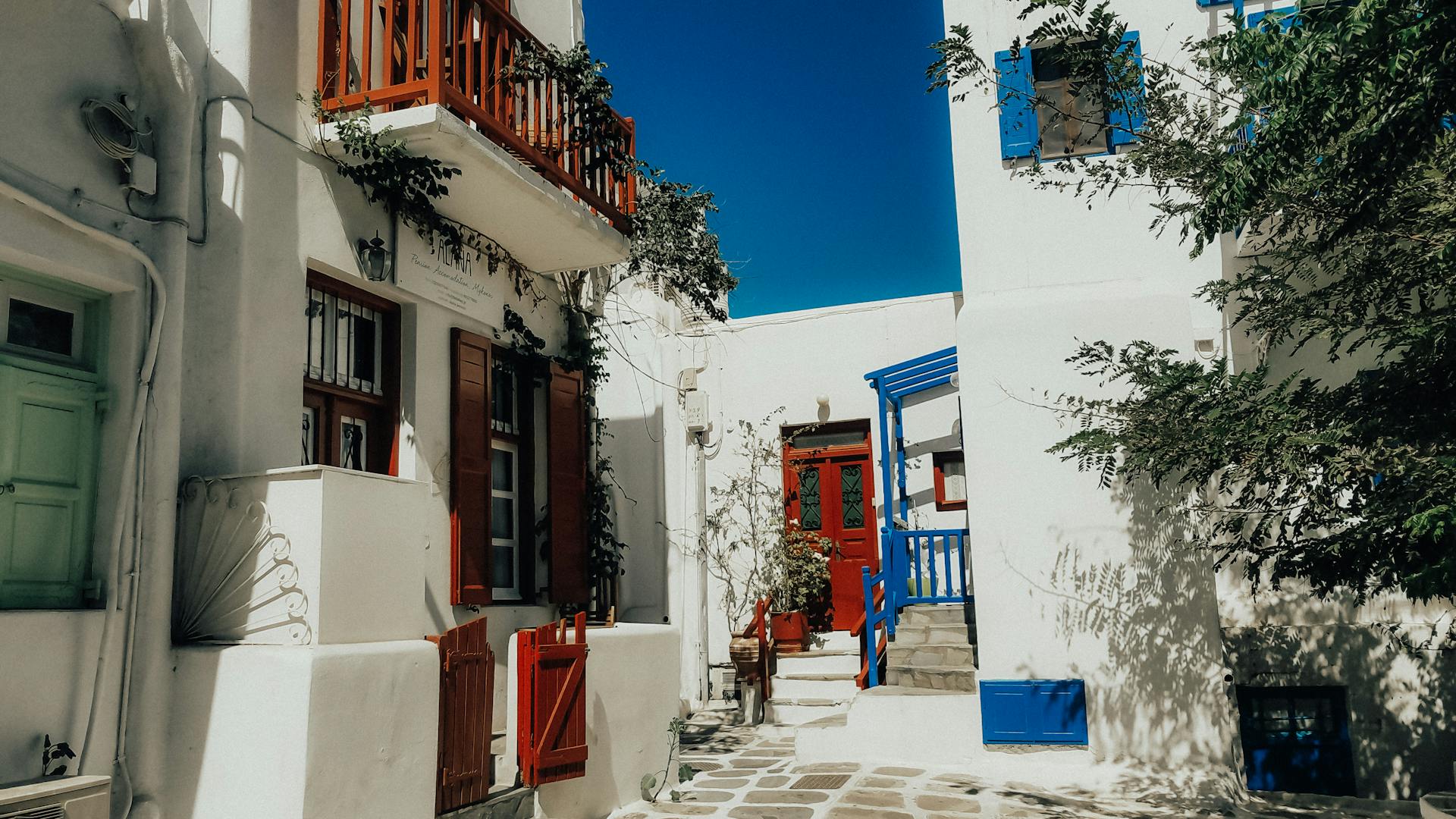 Quaint Greek street scene in Mykonos featuring vibrant blue and red doors against whitewashed buildings.