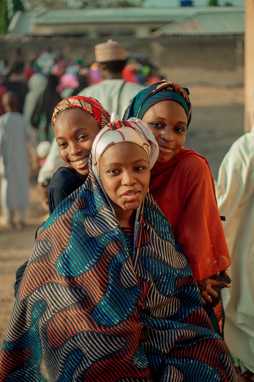 Free Three women in vibrant traditional African clothing smiling outdoors, embodying joy and cultural heritage. Stock Photo