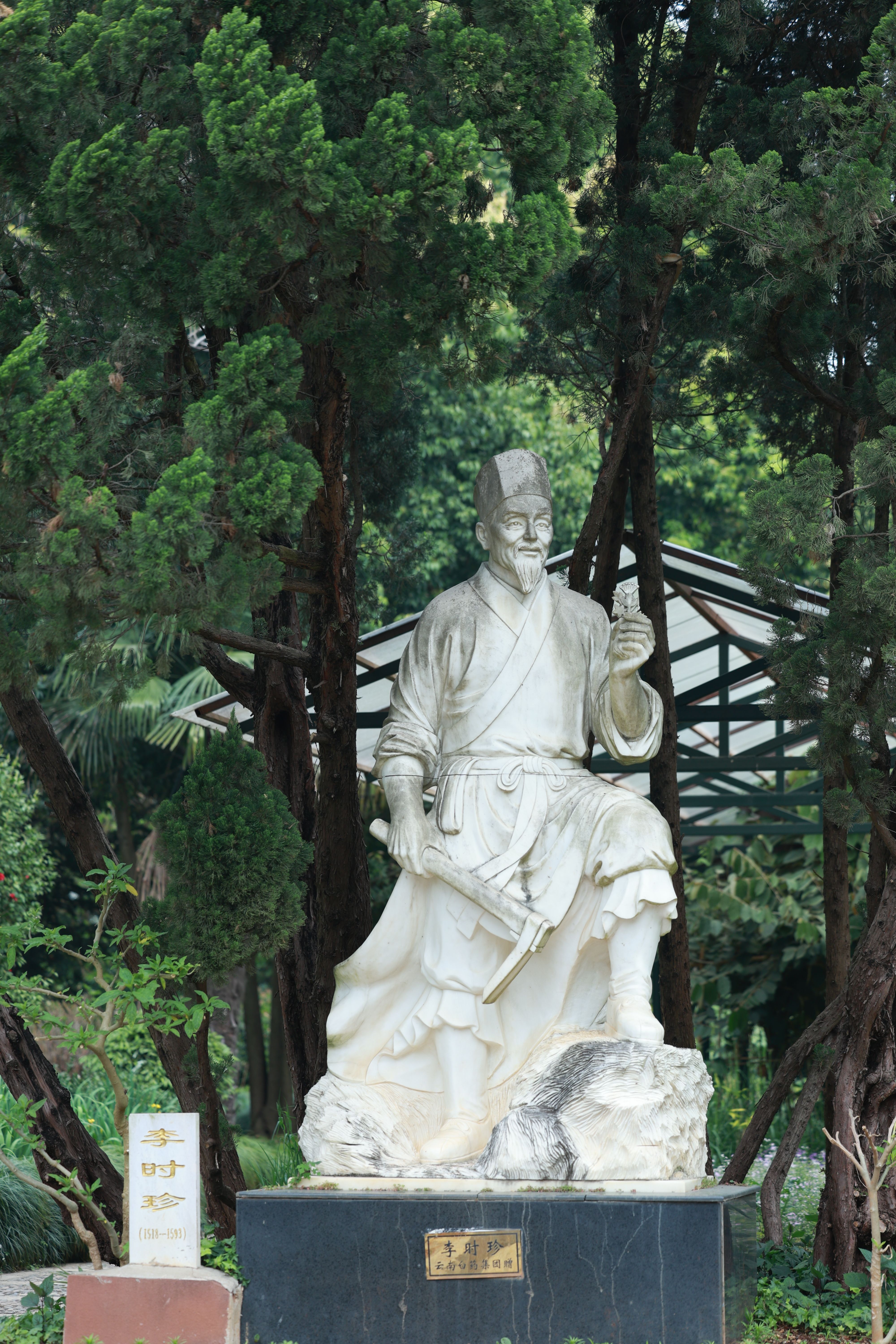 Marble statue of an ancient figure surrounded by lush trees in an outdoor park.