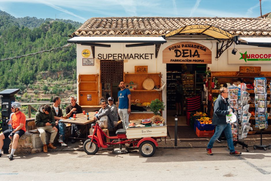 Locales y turistas se reúnen afuera de un encantador supermercado en Deià, Mallorca.