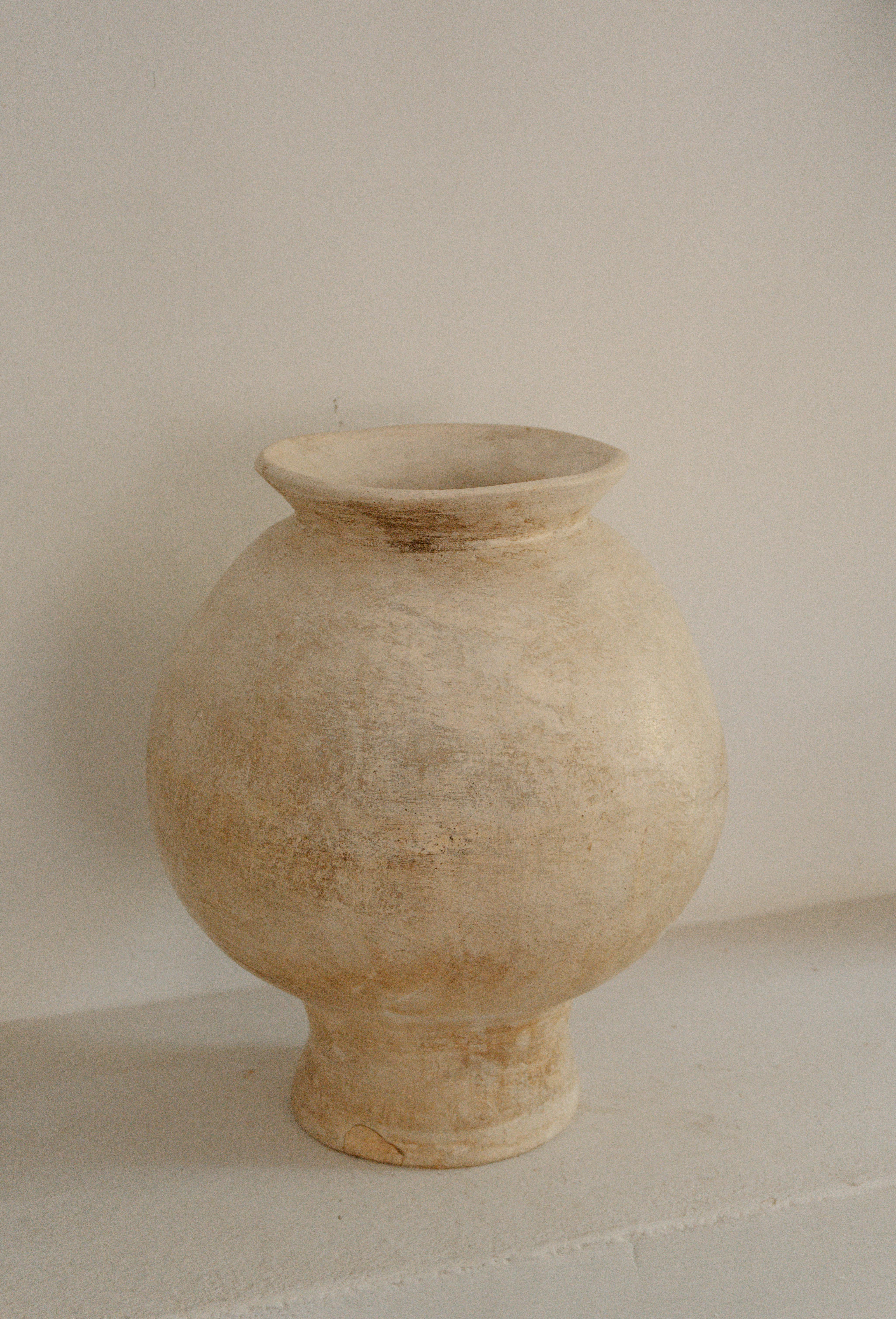 A rustic clay vase with a textured surface placed against a minimalist background, exuding a warm, earthy tone.