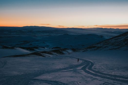 Beautiful snow-covered mountain landscape with vibrant sunset and lone skier.