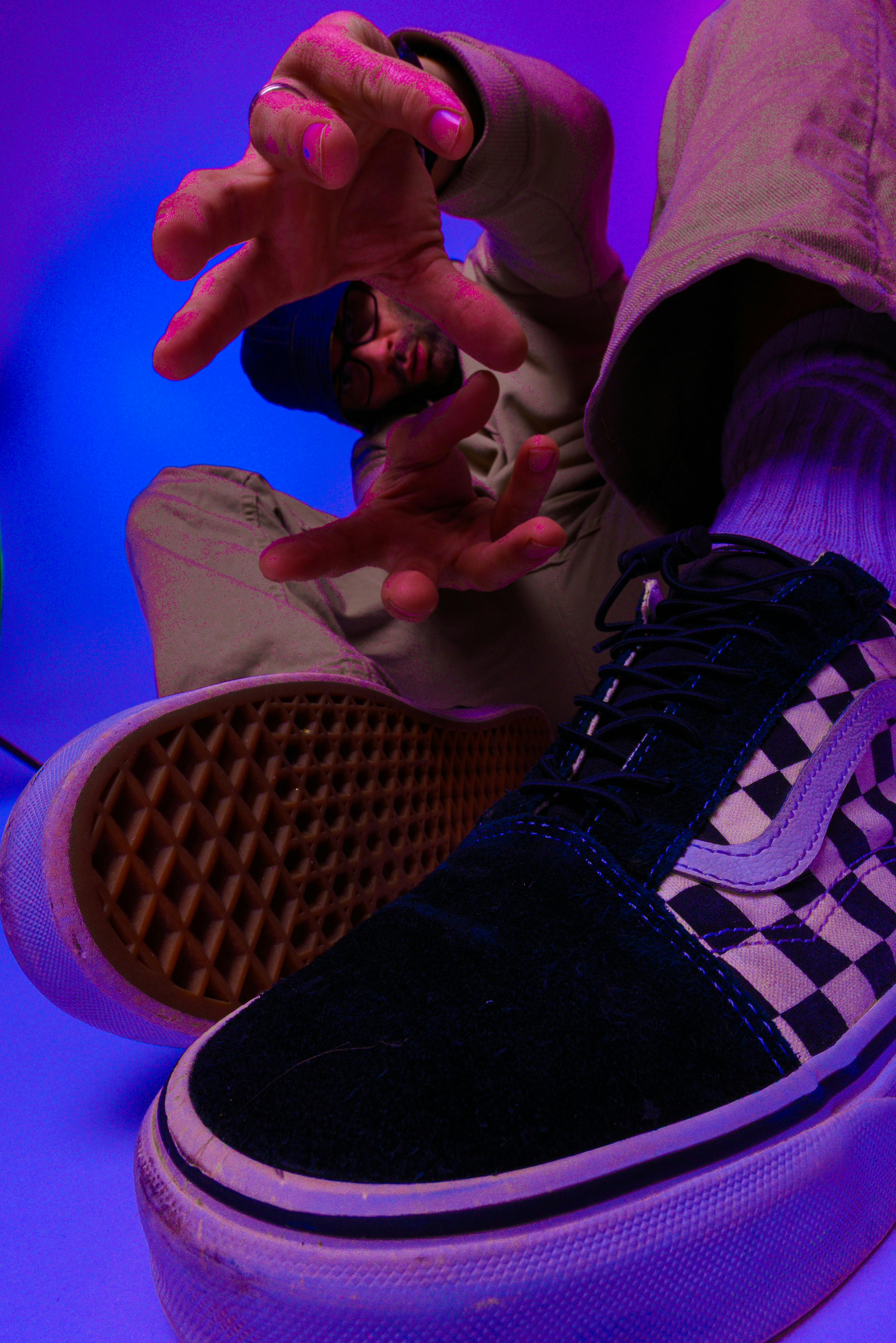 A person reaches out towards the camera with colorful lighting and focus on checkered shoe.