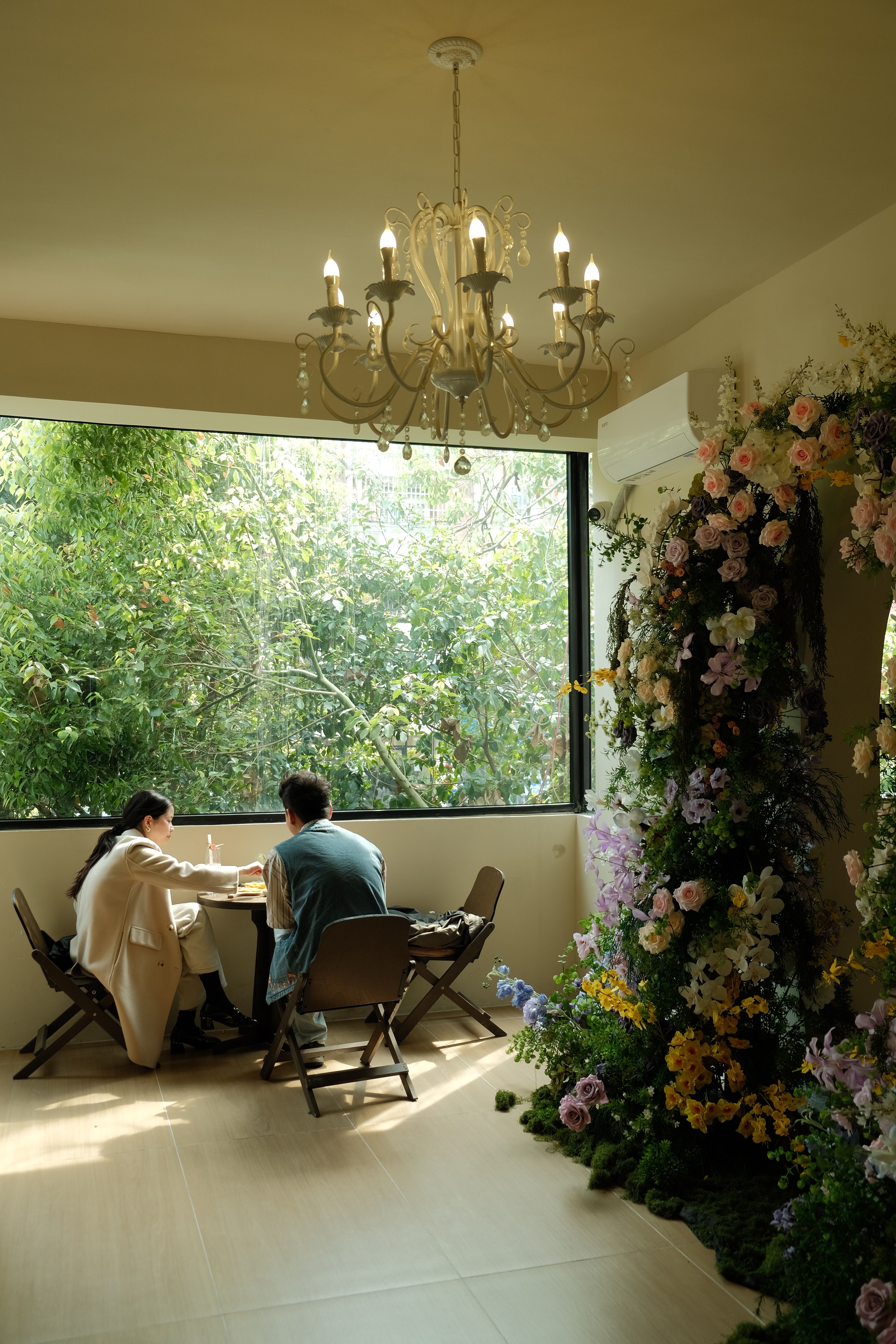 Two people in an indoor cafe with floral decor, enjoying a sunny day.