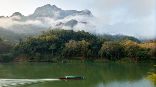 A wooden boat crossing a misty river in northern Laos