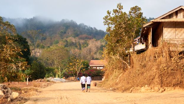 Two children walking on a rural dirt road in a peaceful village, Laos.