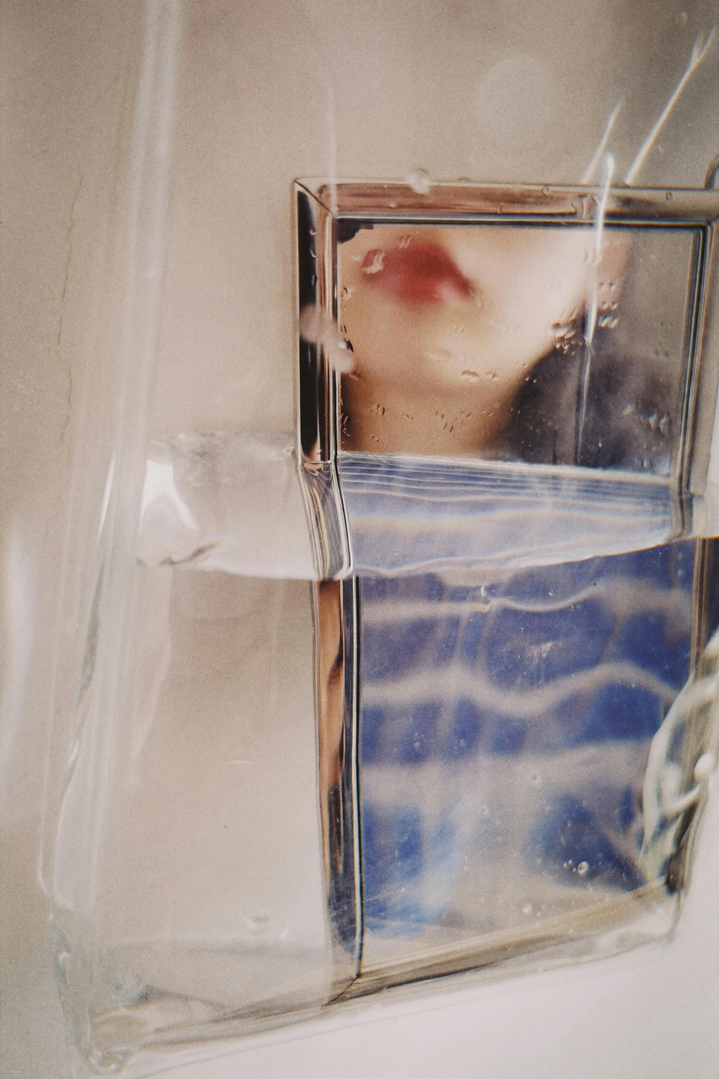 Creative abstract image capturing a face's reflection in water through glass with artistic distortion.