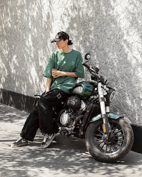 Woman in casual outfit resting on a motorcycle against a wall outside during the day.
