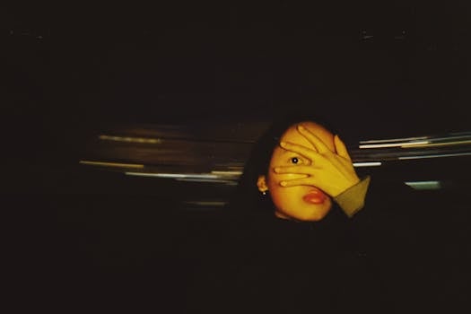 A creative nighttime portrait of a woman covering her face with a hand amid dynamic motion blur.