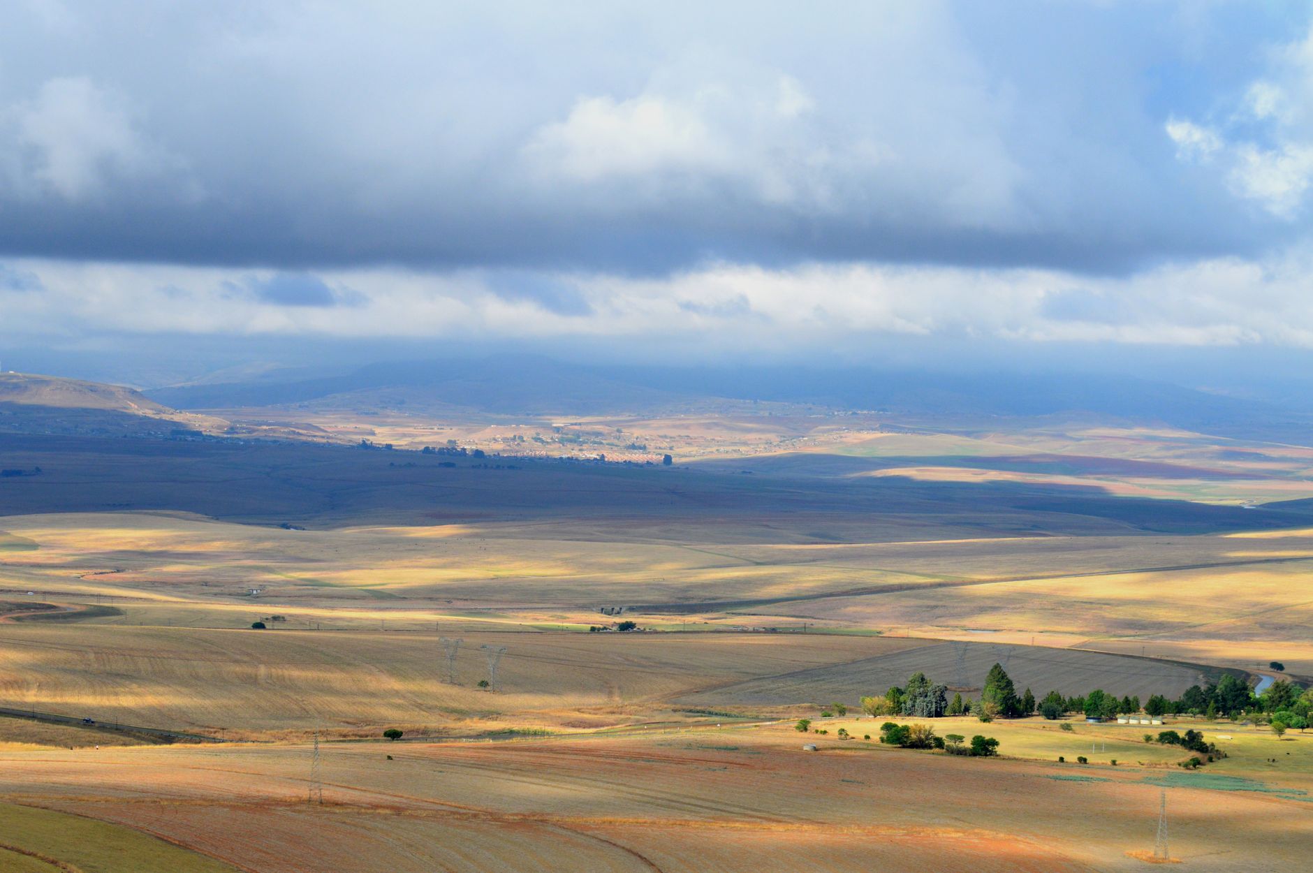 Vast South African landscape with fields under a cloudy sky, showcasing nature's beauty.