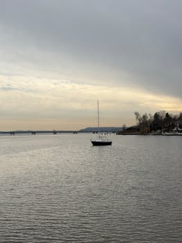 Tranquil image of a lone sailboat on a calm lake during dusk, peaceful scenery.