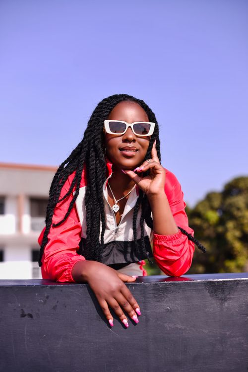 Free Stylish woman wearing sunglasses and red jacket posing outdoors in sunlight. Stock Photo