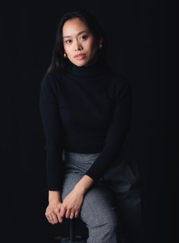 Elegant portrait of a woman in business casual attire seated against a dark backdrop.