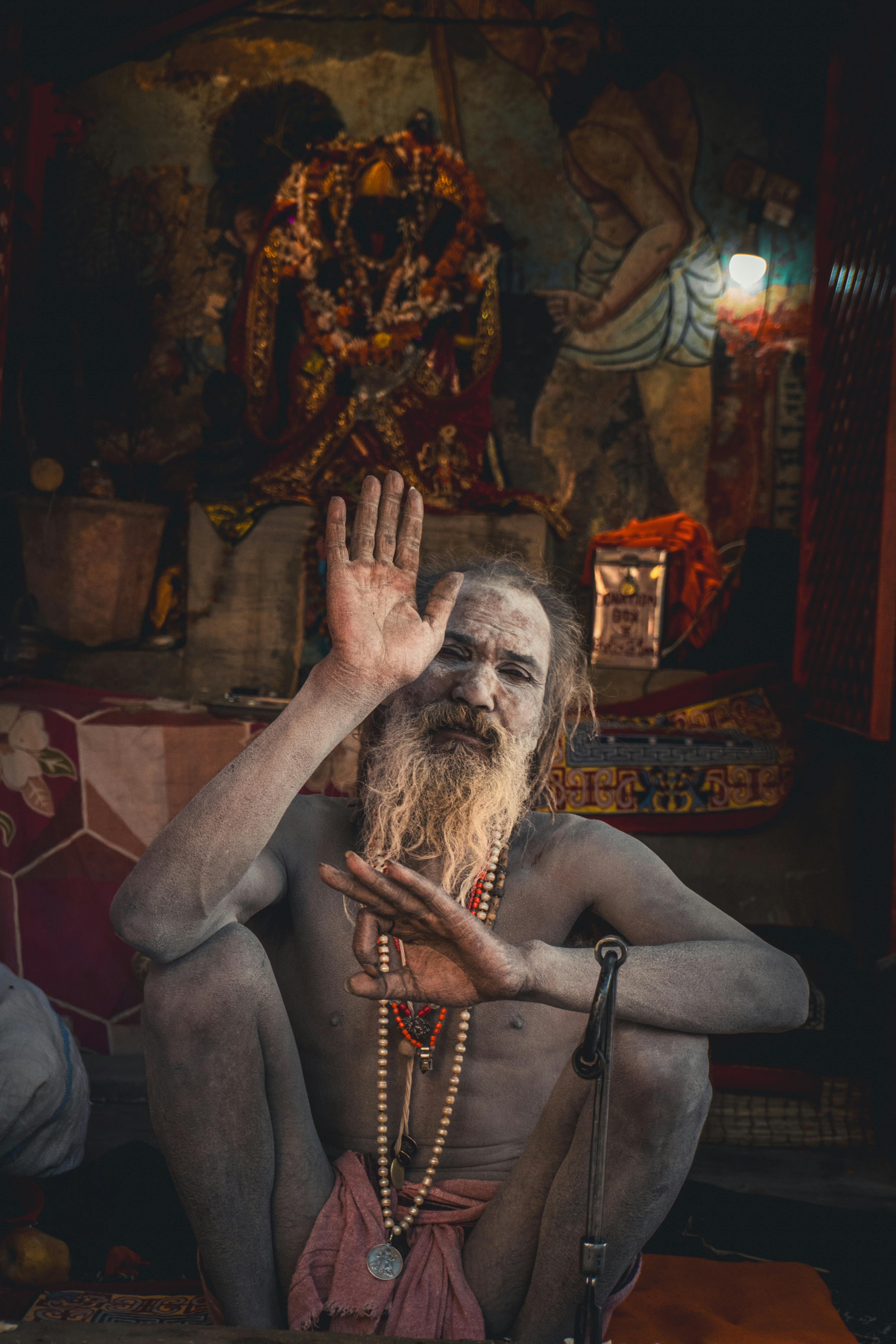 A spiritual guru in traditional attire performs a blessing gesture against a cultural backdrop.