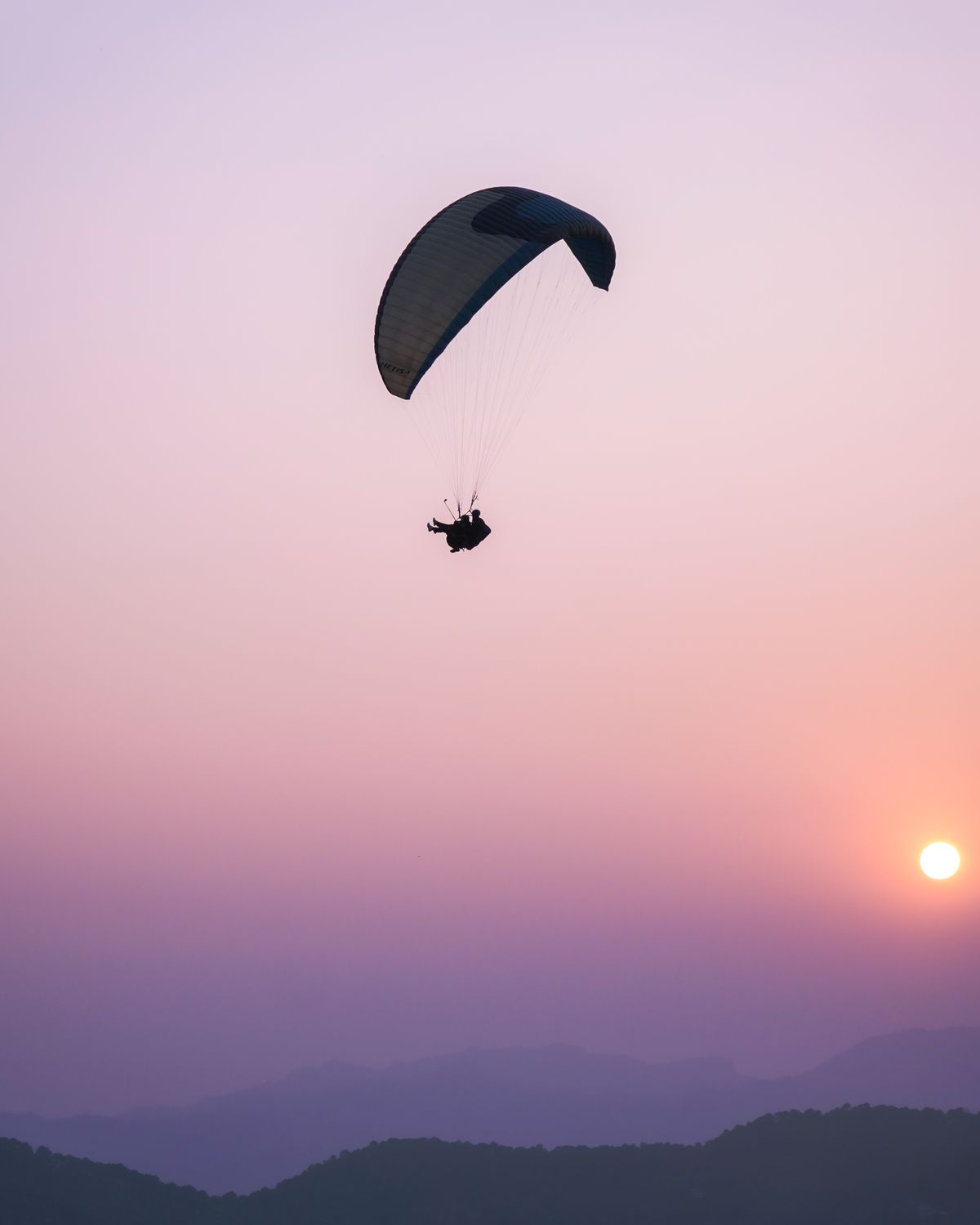Silhouette of a paraglider soaring against a vibrant sunset over mountains Silhouette of a paraglider soaring against a vibrant sunset over mountains